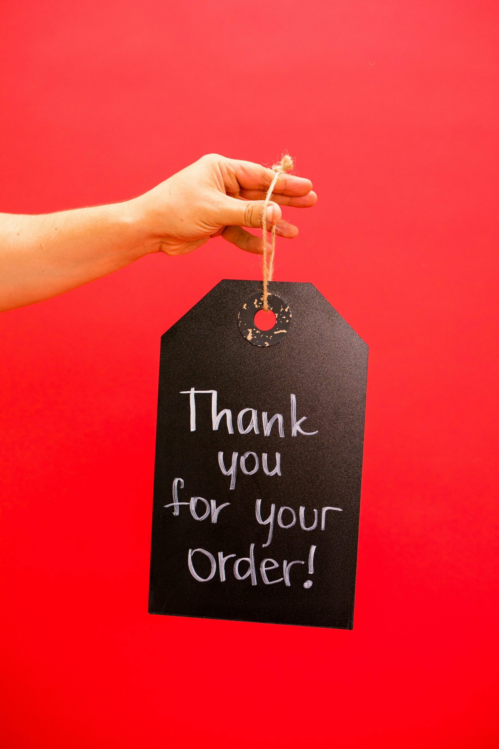 A hand holds a black tag with 'Thank you for your order' on a vibrant red background.